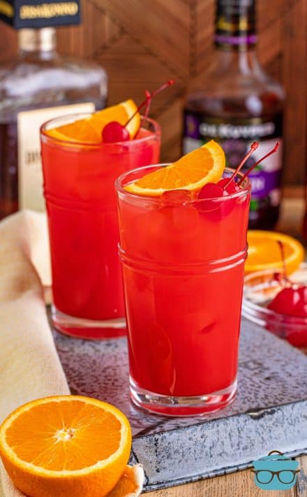 Alabama Slammer in two cups on metal tray with alcohol in background.